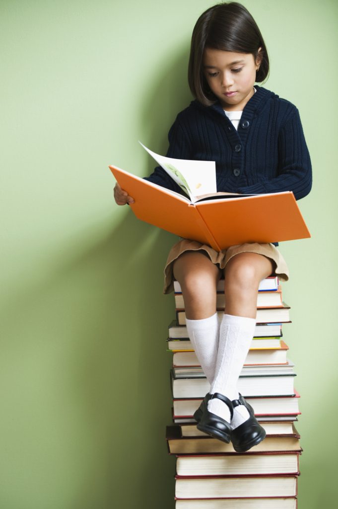 Girl sitting on a tower of books reading